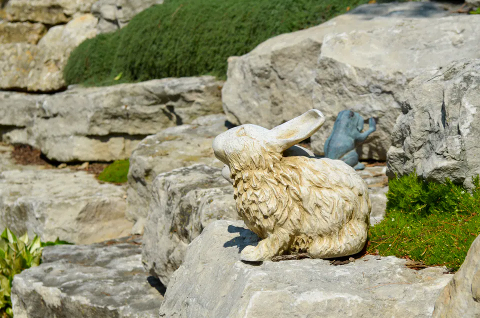 Garden ornament set into a limestone boulder wall with clipped groundcover, mulch, and evergreen planting.